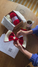Load and play video in Gallery viewer, hands making a crocheted Christmas Bow Decoration in red and cream

