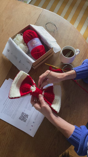 hands making a crocheted Christmas Bow Decoration in red and cream